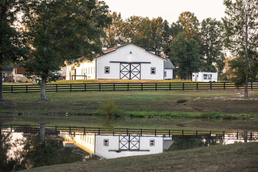A white barn sits on a farm by a lake