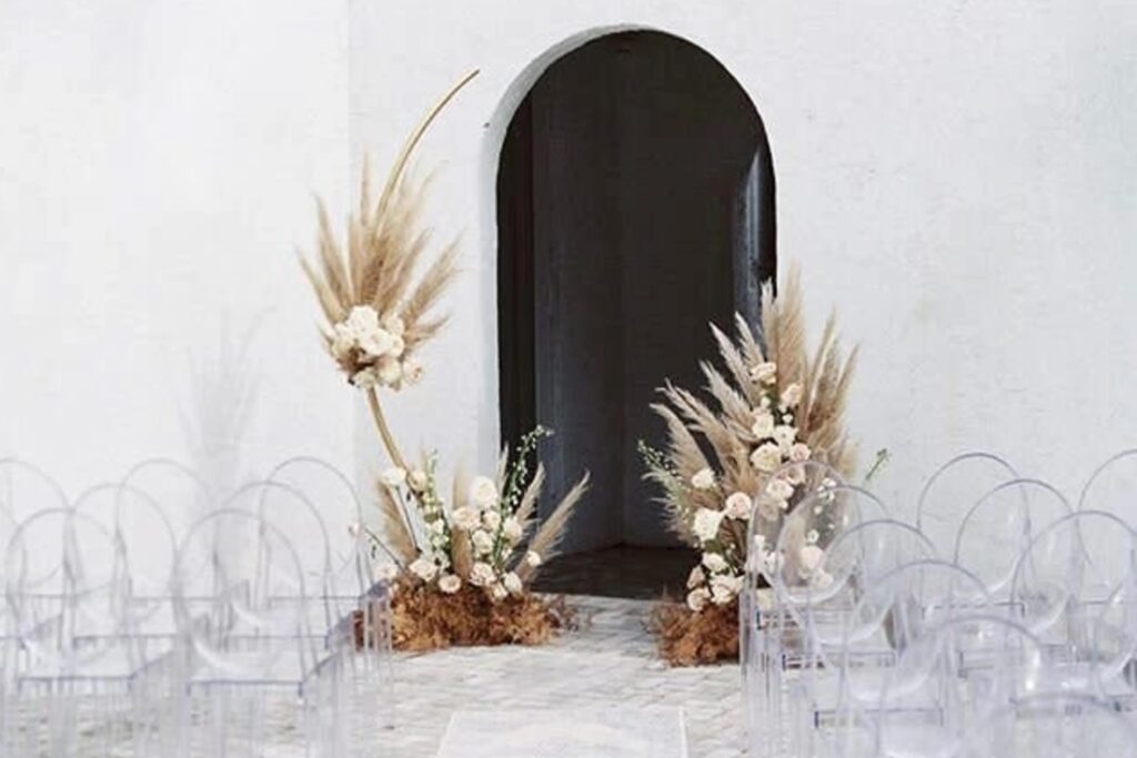 Plexiglass chairs line a wedding ceremony aisle that leads to a bohemian altar decorated with white and tan florals