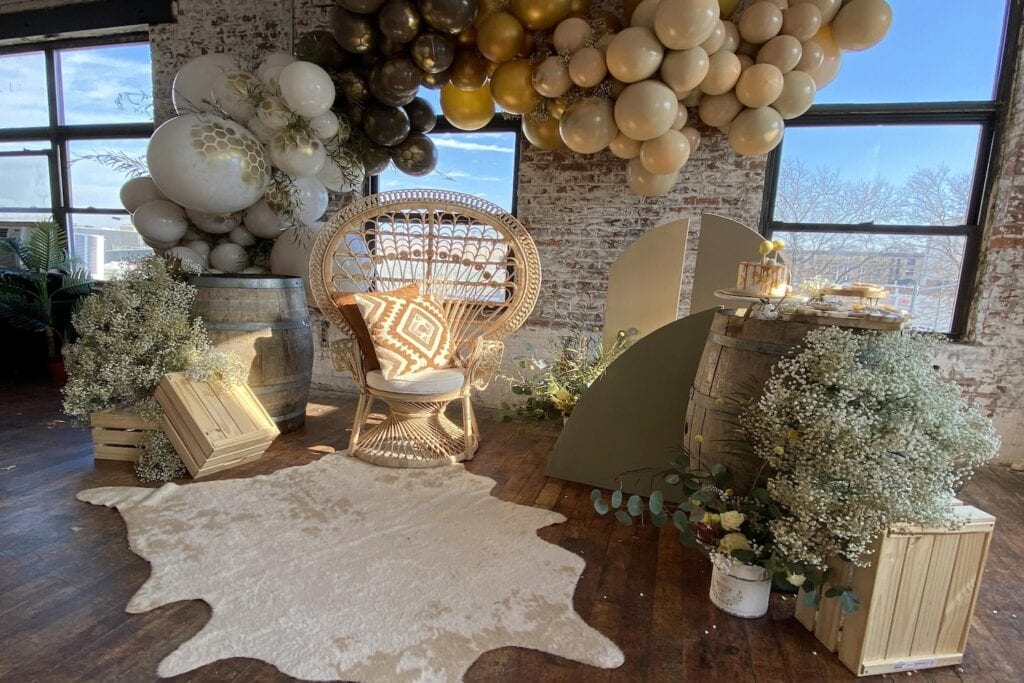 A wicker chair sits next to wine barrels and fall-themed decor at a baby event