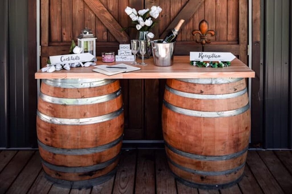 Wine barrels are used as the base of a table holding champagne and signs directing guests to a reception