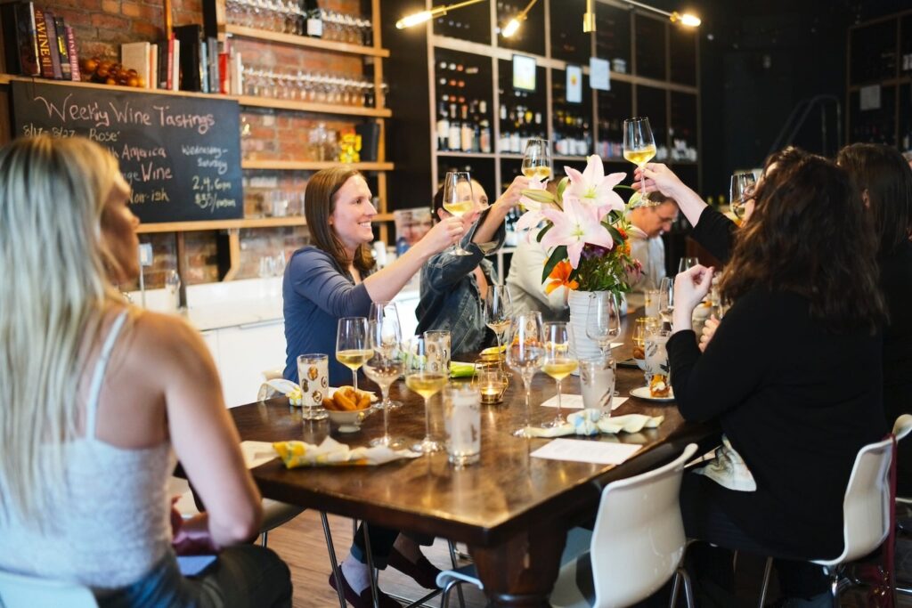 Women gather around a table toasting with glasses of wine at a wine tasting event