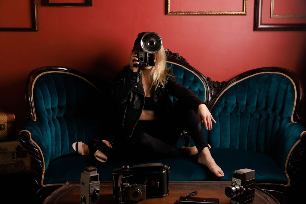 A woman sits on a dark blue velvet couch surrounded by 20s-era cameras
