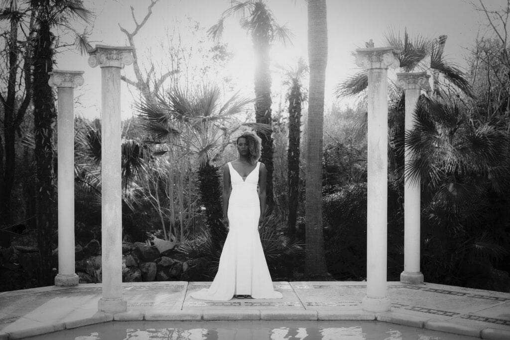Bride standing by pool in tropical location looking seriously at camera