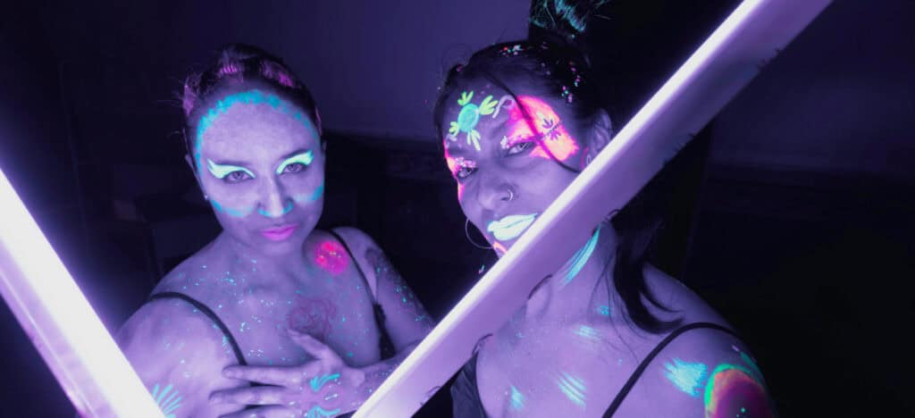 Women in neon makeup holding black lights that are making them glow