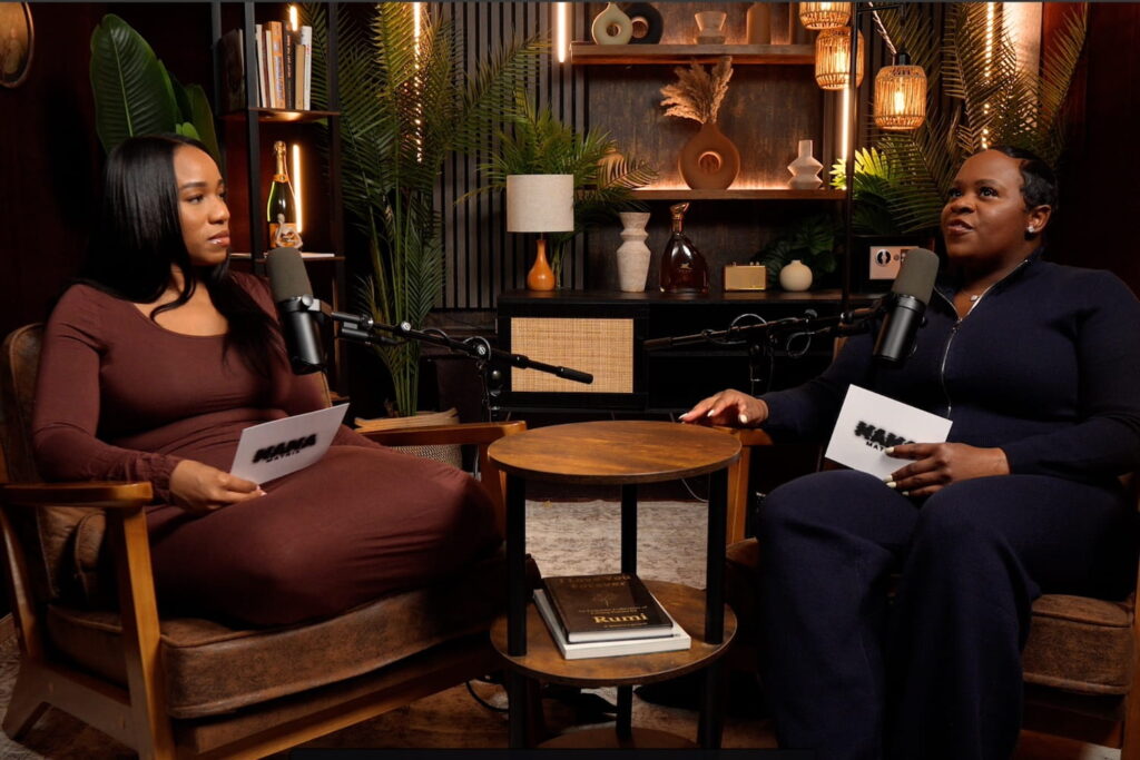 Two women in front of microphones recording a podcast in a cozy studio space