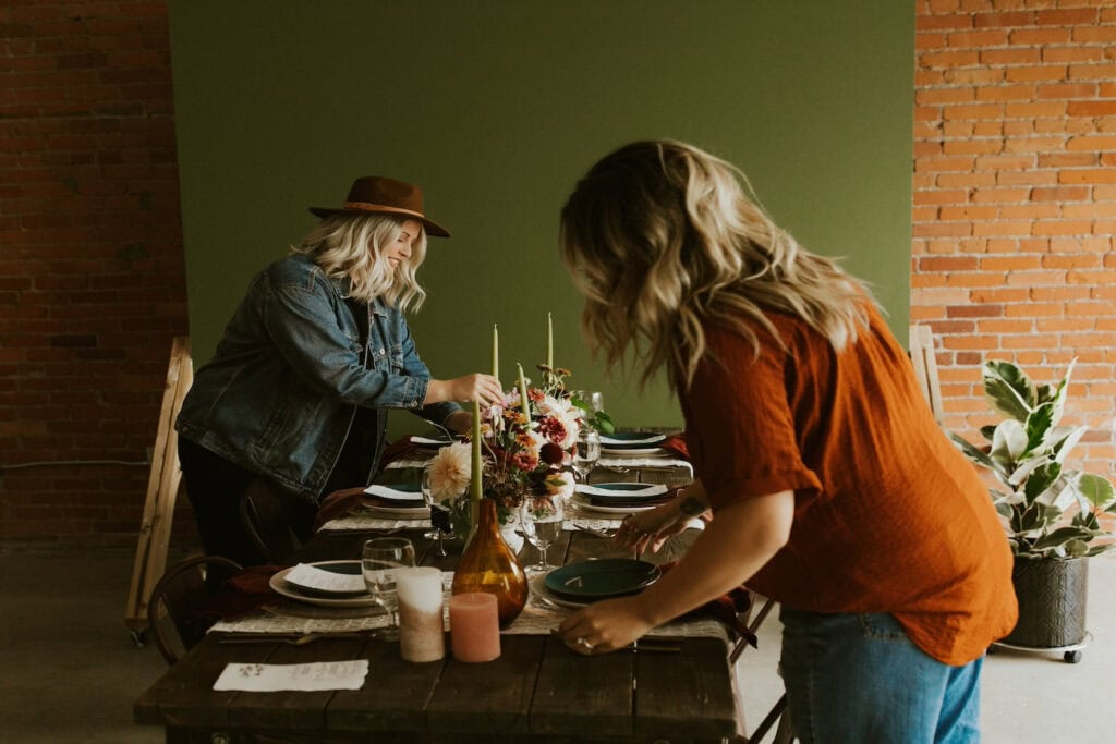 Women set a holiday table with flowers, candles and fall decor