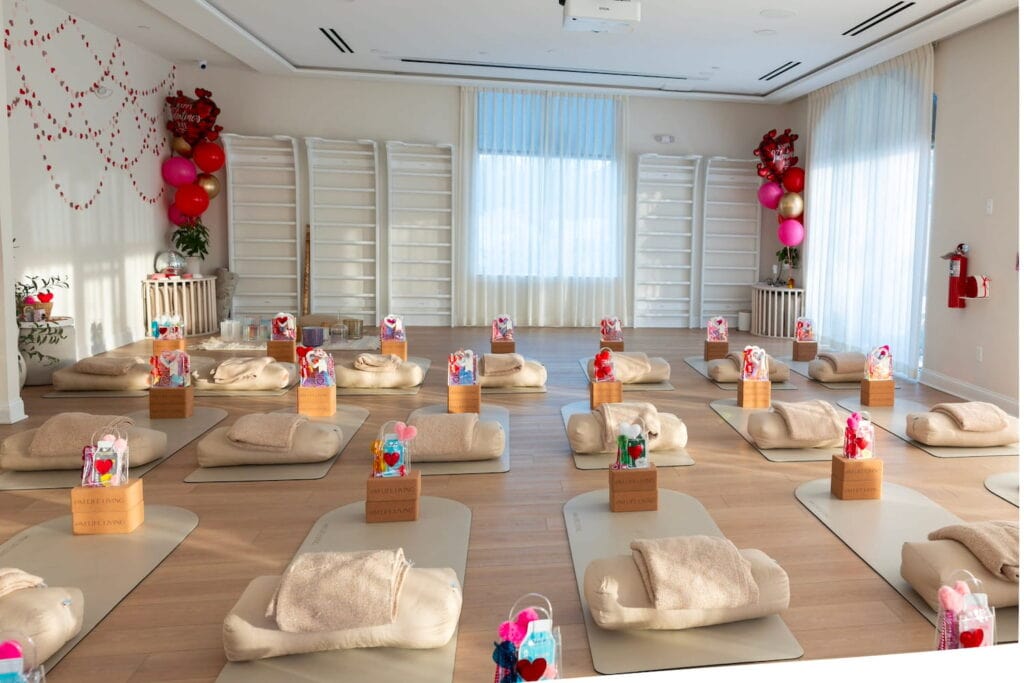A small, brightly lit event space is set up with yoga mats and party balloons with gift baskets at the foot of every mat