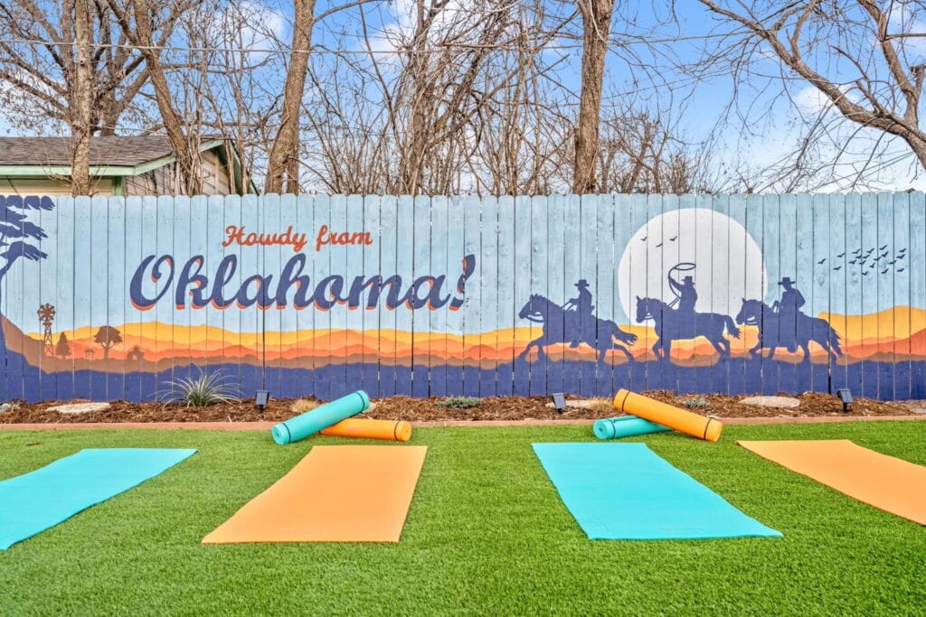Yoga mats set up on the lawn of a backyard by a fence with a mural of cowboys on horseback