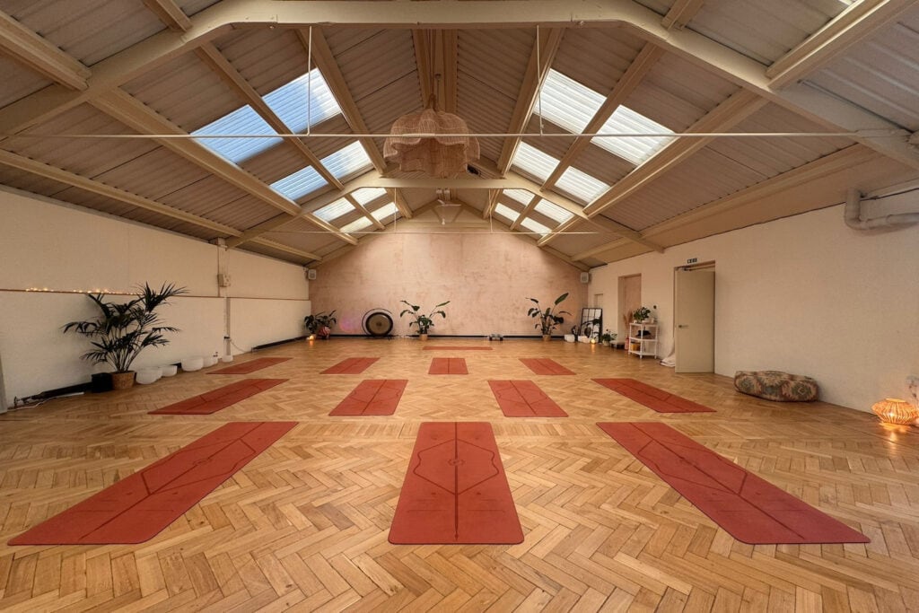 A warmly-lit space with high ceilings and skylights is set up with yoga mats and dim lights