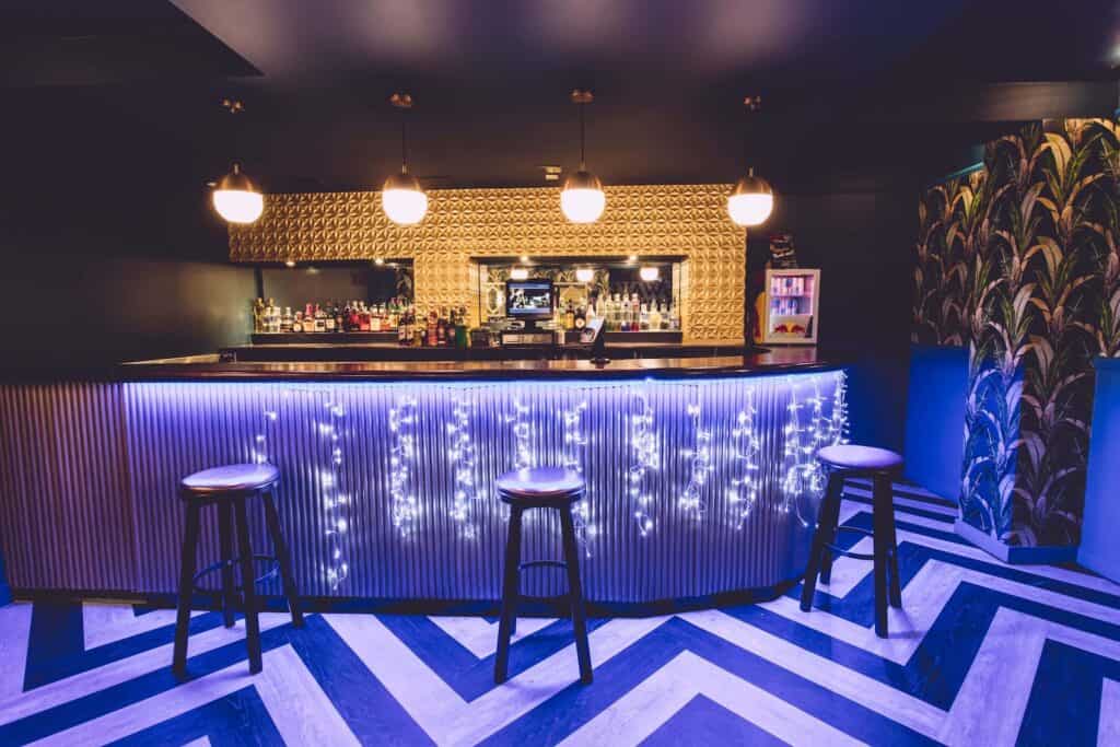Stylish bar with stools, string lights, and patterned floor, perfect as a stag party venue.