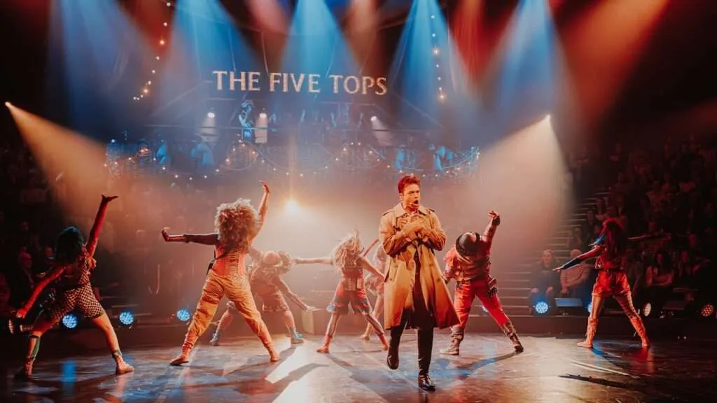Come Alive London The Greatest Showman immersive musical with cast performing under spotlights in front of a Five Tops sign