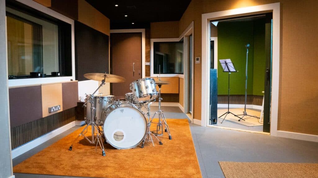 Modern music studio with drum kit, vocal booth, and acoustic panels.