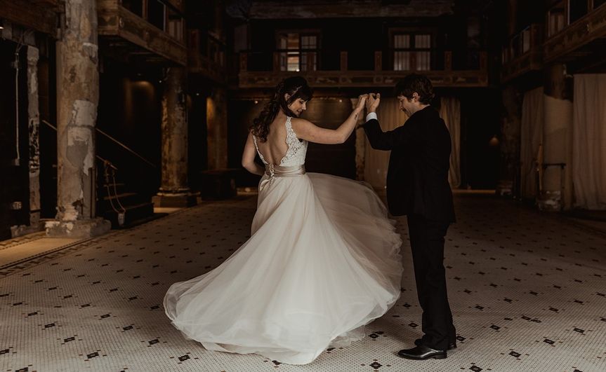 Bride and groom dancing at a wedding reception venue with elegant, rustic decor and a tiled floor.