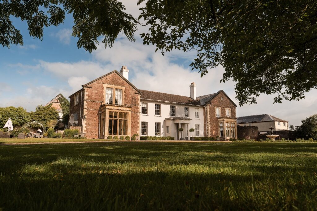 Sprawling mansion to rent with large windows, manicured lawn, and classic architecture under a blue sky.