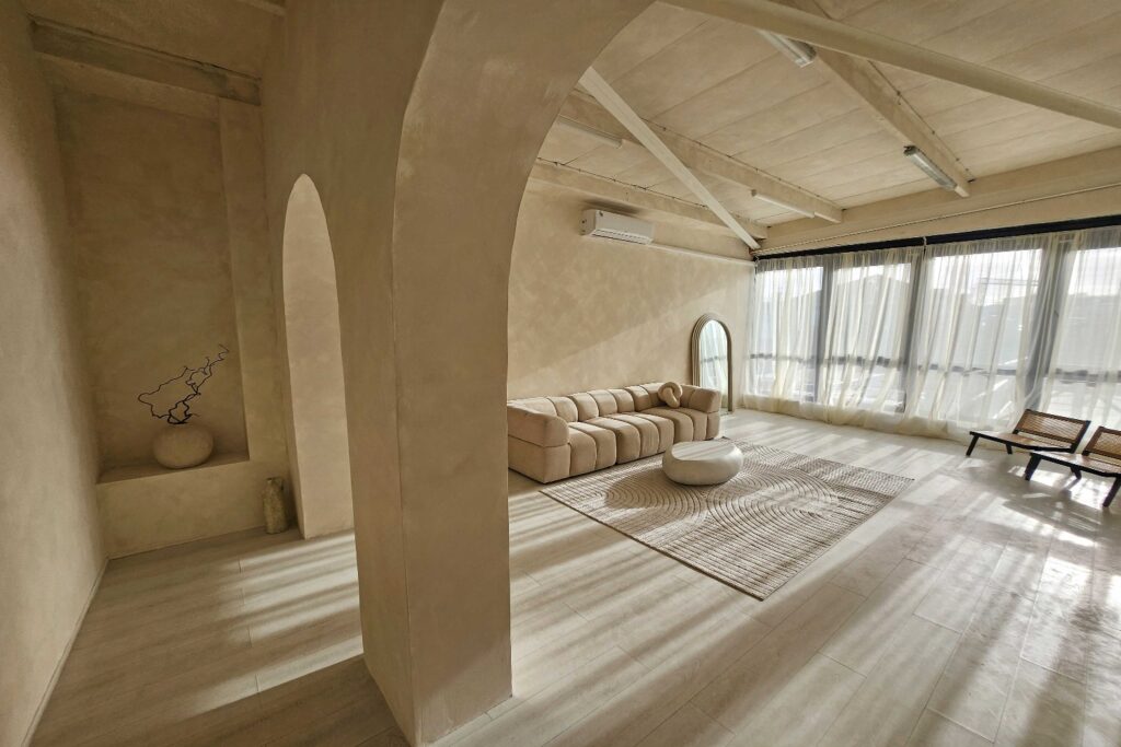 Spacious photo studio with arched walls, neutral decor, large windows, beige sofa, and natural light filling the room.