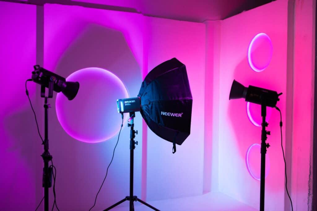 Photo studio with three lights, softbox, and pink-purple lighting setup against a white wall with circular accents.