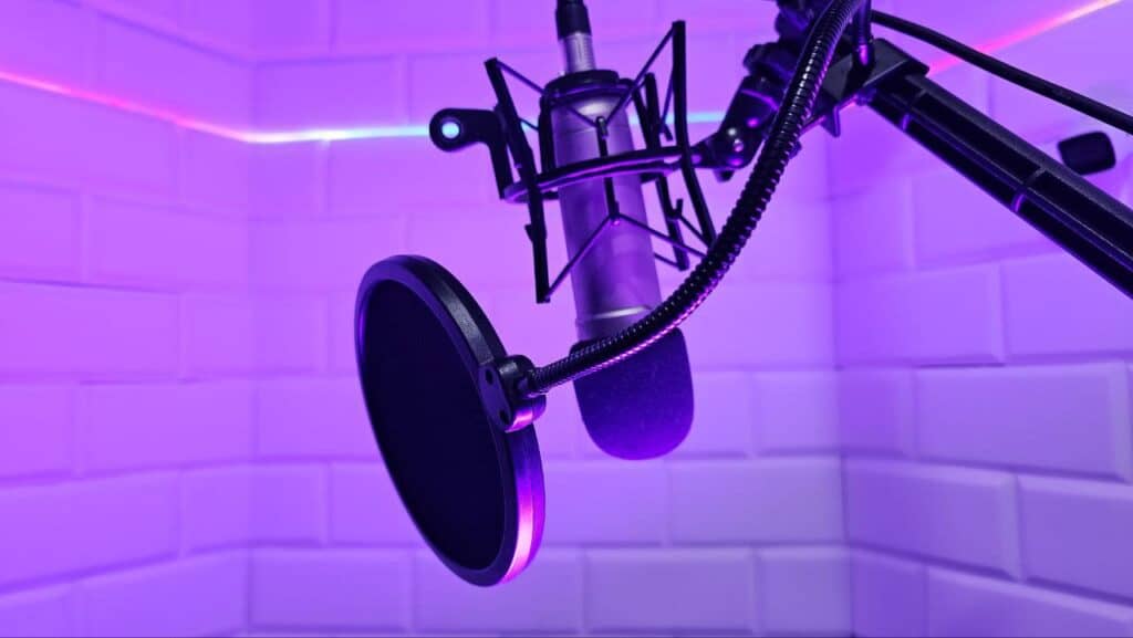 Microphone with pop filter in a neon-lit recording booth music studio.