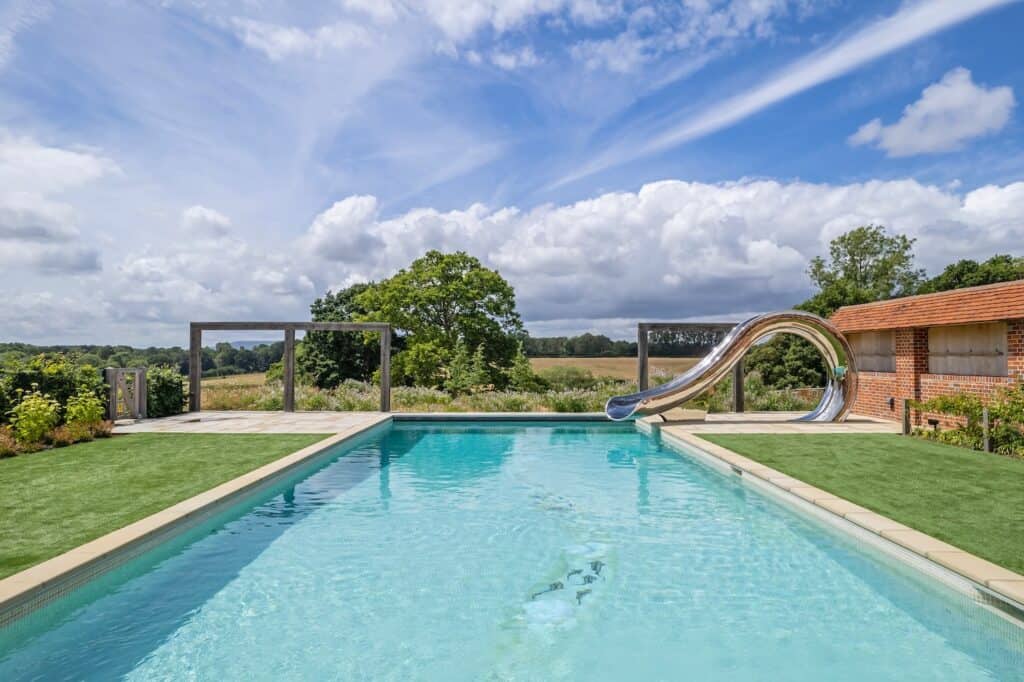 Outdoor stag party venue with swimming pool, water slide, and countryside views under a bright blue sky.