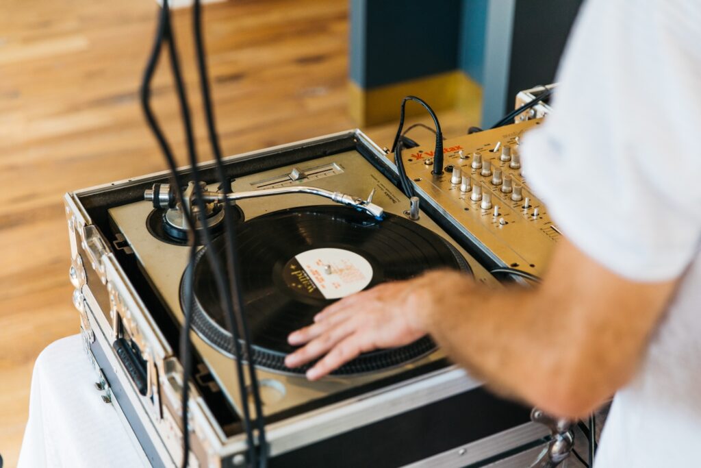 DJ spinning vinyl records at a wedding reception venue, with turntable and mixer on a wooden floor.