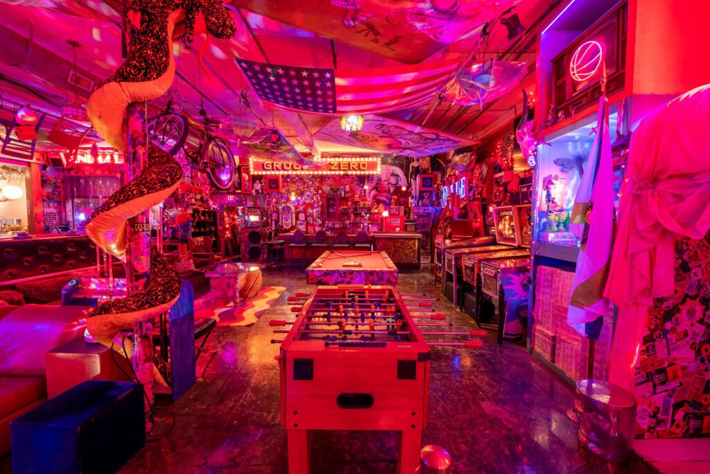 A retro arcade game venue with bright neon lights, pool and football tables and a bar.