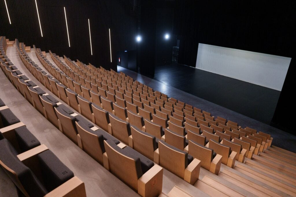 250-seat modern auditorium with tiered wooden seating viewed from the stage, available to hire by the hour on Peerspace