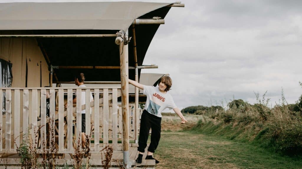A boy on the patio of a tent-style bungalow at a glampsite in the countryside.