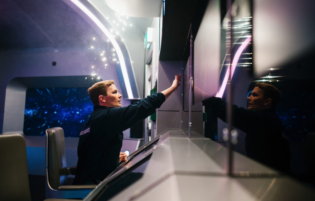Bridge Command London with crew member in spaceship uniform operating control panels with starfield window in background