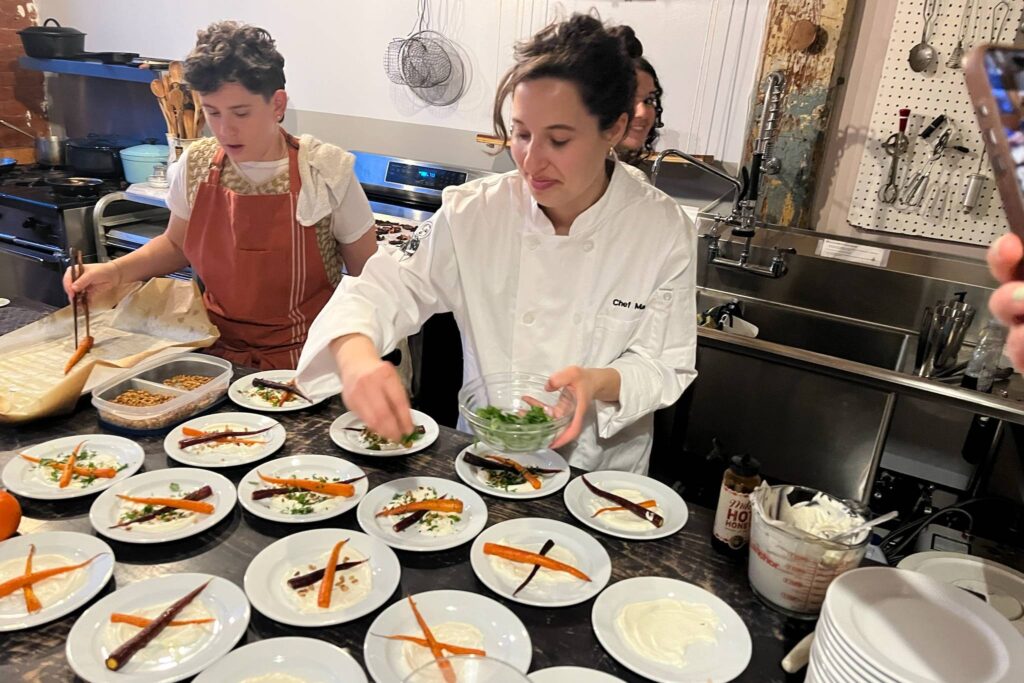 A chef and her team preparing plates in a commercial kitchen