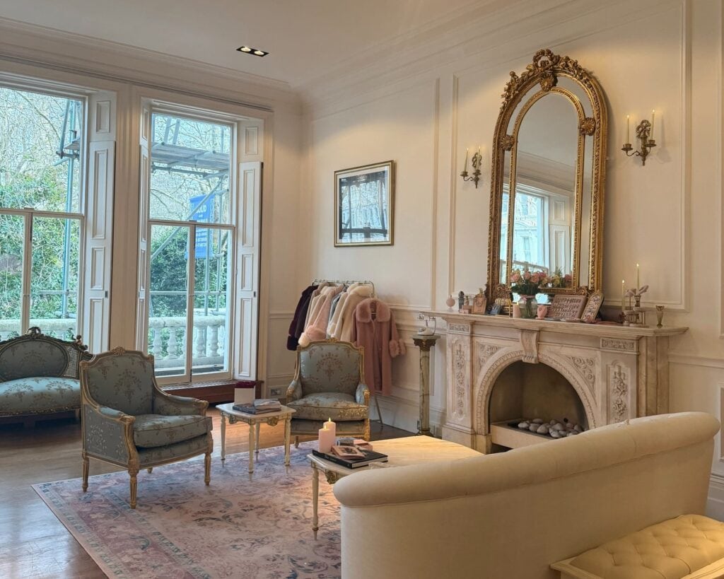 Classical London photo shoot set with gilt mirror, marble fireplace and Louis XV armchairs, styled with a rail of faux fur coats