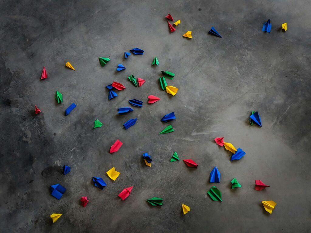 Colorful paper planes laying on a concrete floor.