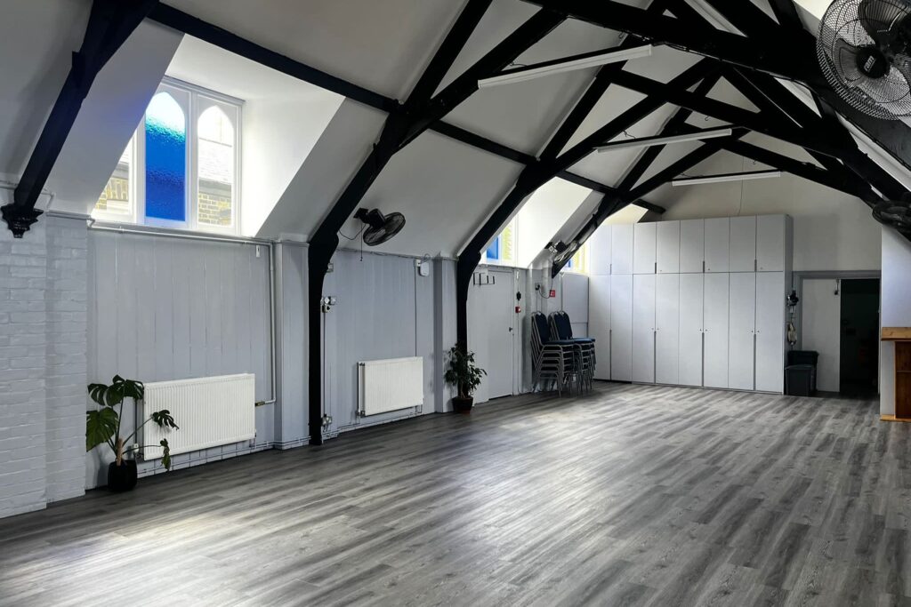 View of a converted church venue with stacked chairs and vaulted ceilings with exposed black beams.