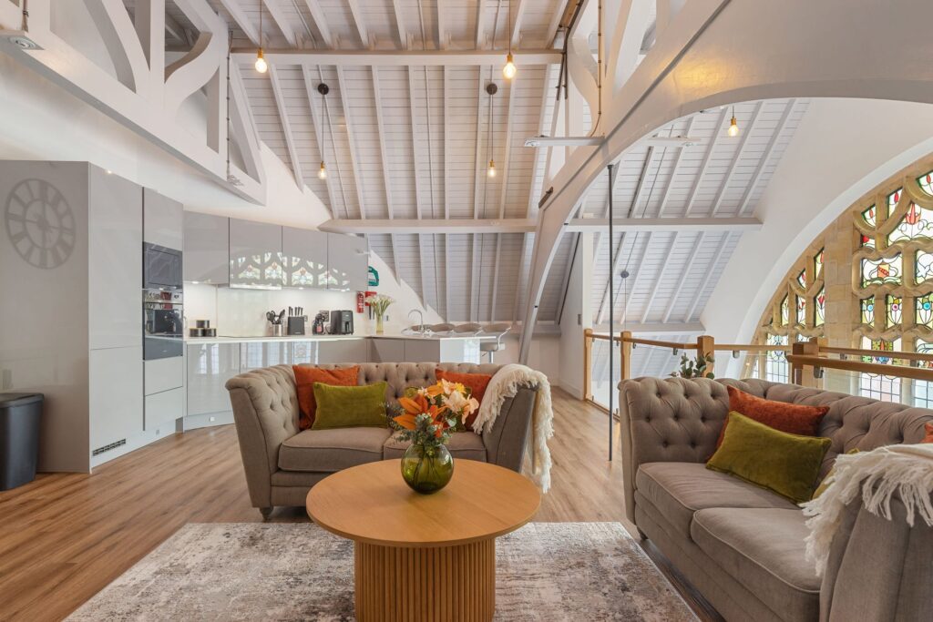 Lounge in a converted church with white wooden ceilings and an ornate stained glass window