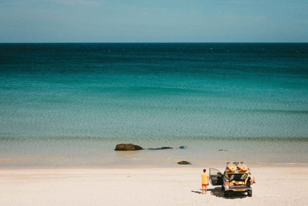 Beach in Cornwall with a parked car carrying surfboards