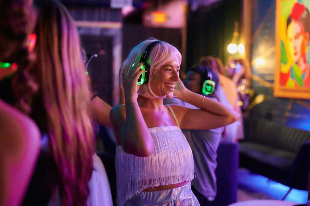 A woman with silent disco headphones and a wig dances among a group of people.