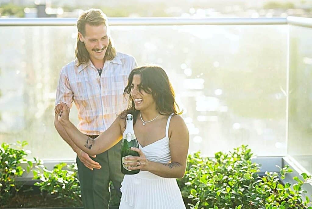 couple standing on a balcony opening champagne