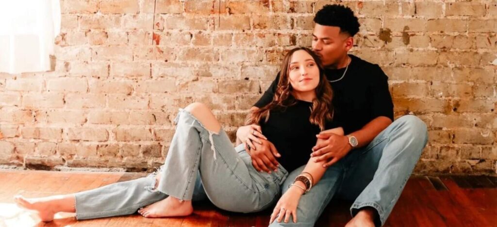 couple holding each other in front of exposed brick wall
