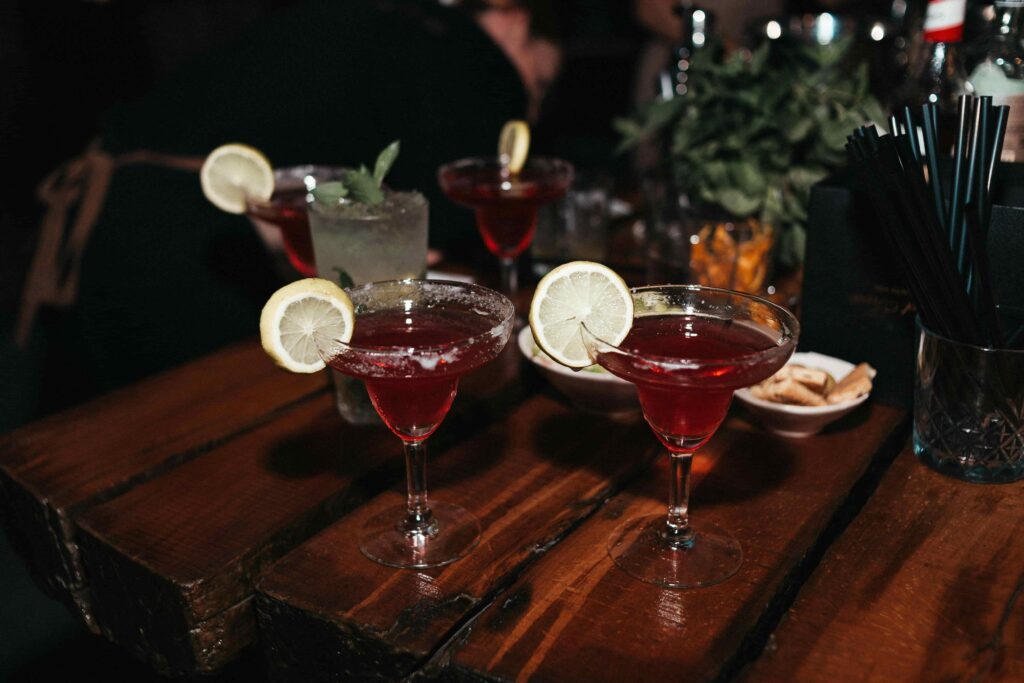 Four dark-red cocktails with lemon slices on a wooden table.