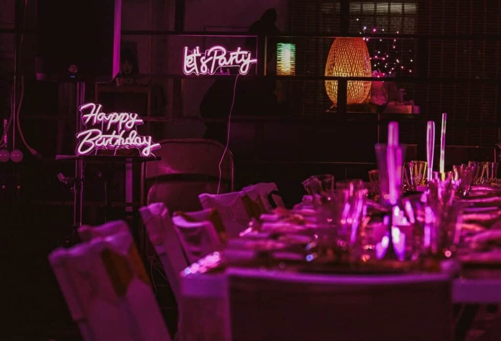 Dark dinner venue with glowing neon signs and a large set table.