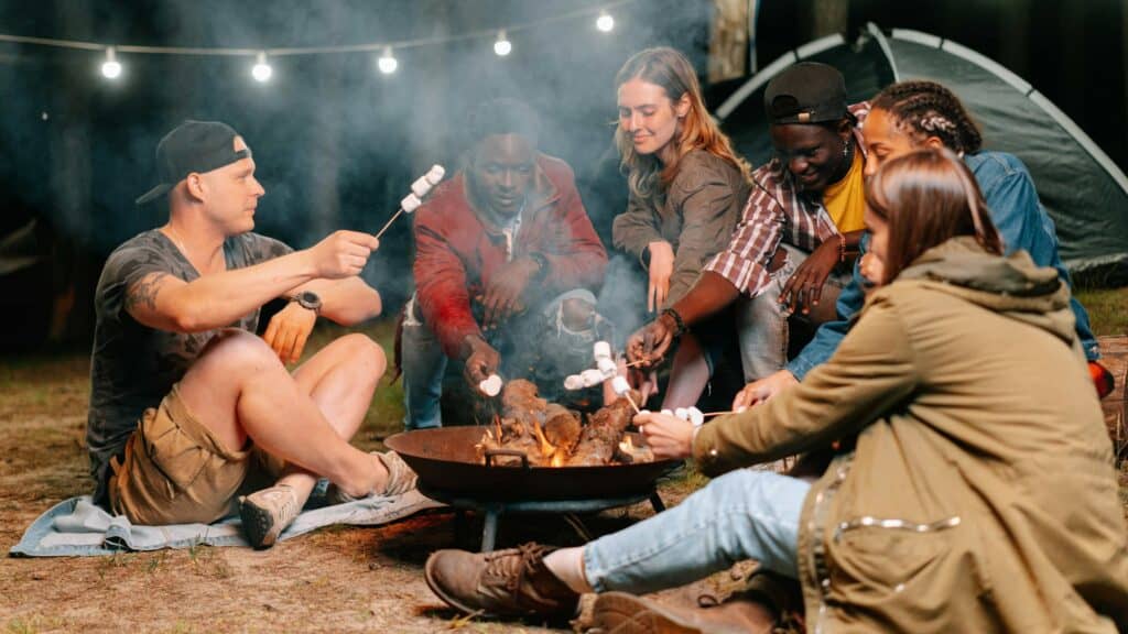 A group of friends grilling marshmallows over a fire pit at a campsite.