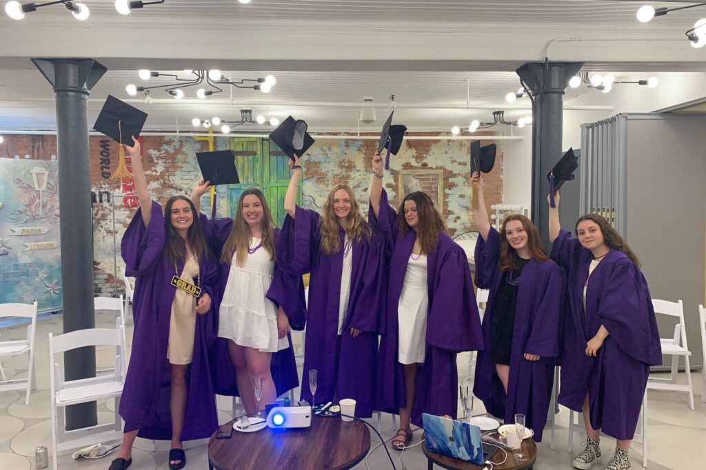 A group of young women lifting in graduation gowns lifting their cap for a photo