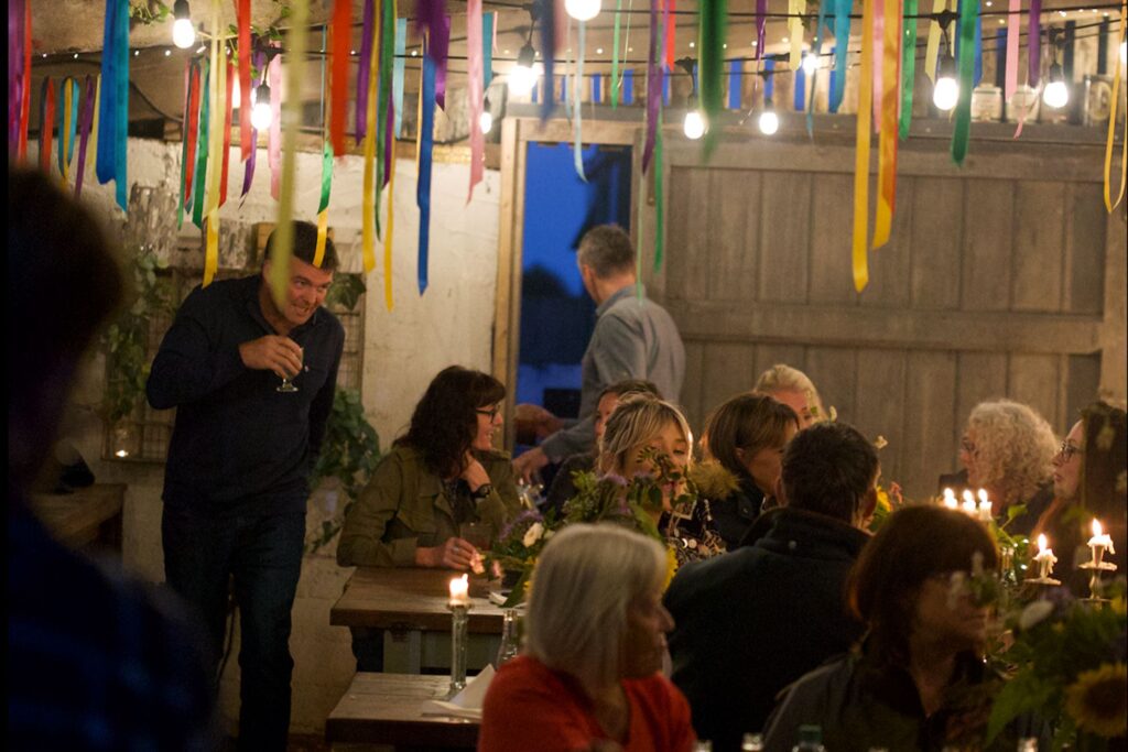 Group of people sitting on tables over drinks with a garland and light decorations on the ceiling