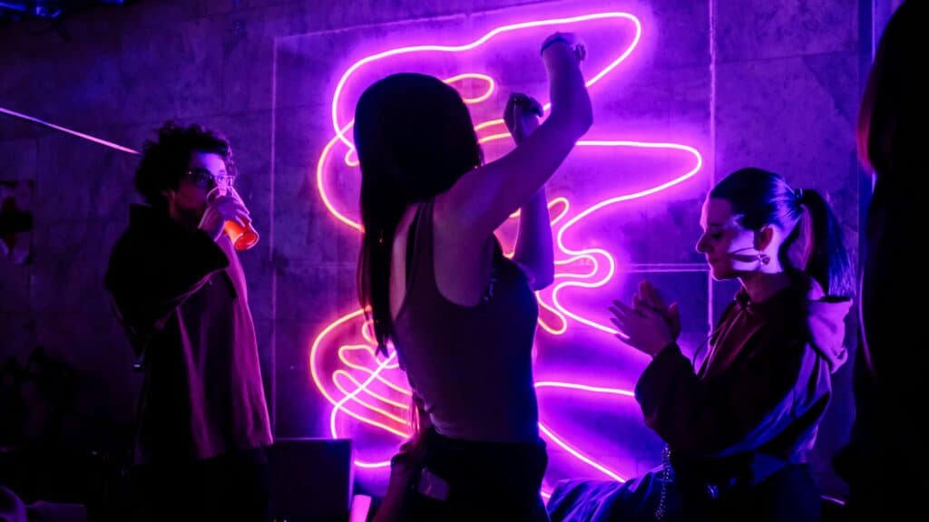 A group of people dance in a dimly lit room with glowing neon signs.