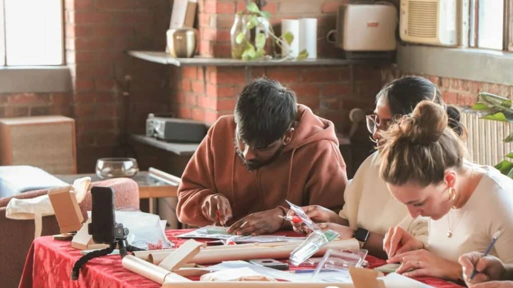 A group of young adults having a crafts session inside a brick-walled room.