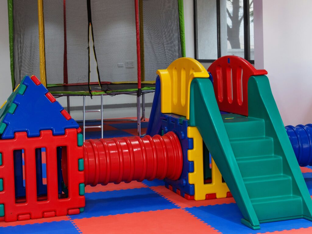 A colorful indoor playground for kids with a trampoline in the background.