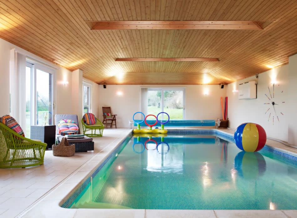 Indoor private swimming pool with vaulted wooden ceiling, colourful lounge chairs and pool toys, set up for a children's party hire