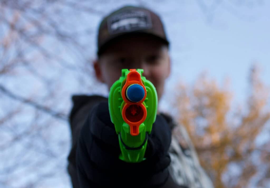 A boy with a cap pointing his Nerf blaster gun at the viewer.