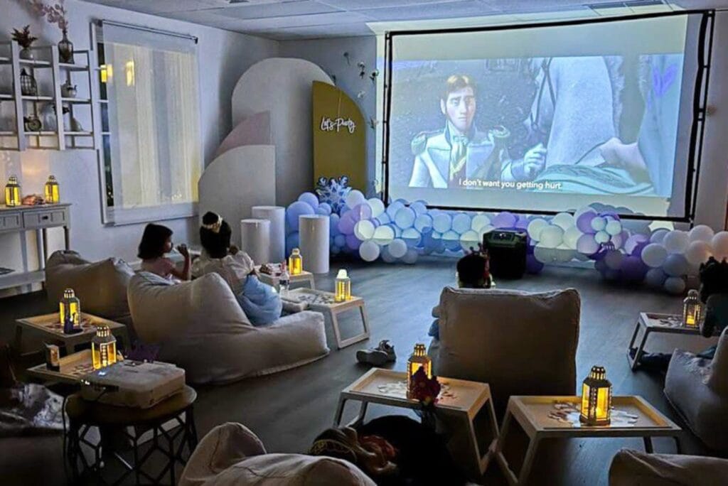 kids sat in front of a projector screen in room decorated with balloons