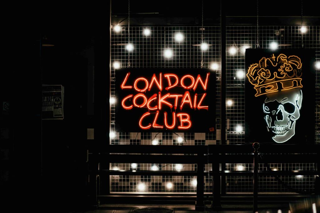 View of a grungy London Cocktail Club with two bright neon signs.