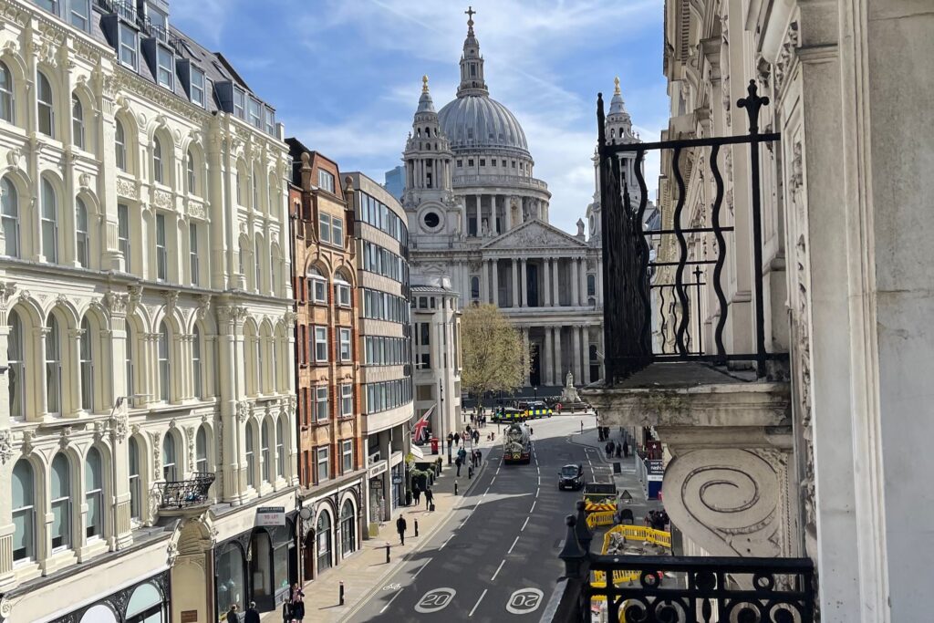 View of St. Paul's Cathedral in London and a sunny street with old buildings from a top-floor balcony.