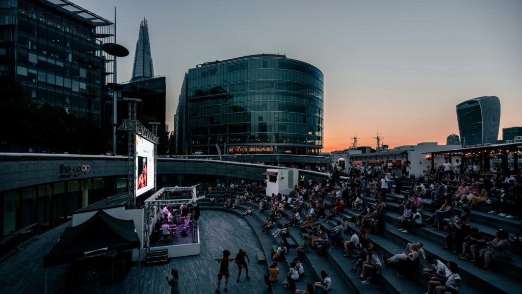 An outdoor screening of a movie on a London rooftop with views of the Shard and the Sky Garden at sunset.